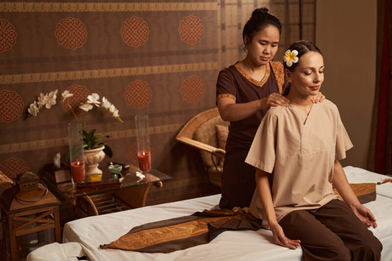 Experienced Thai masseuse palm pressing client upper trapezius region during treatment session