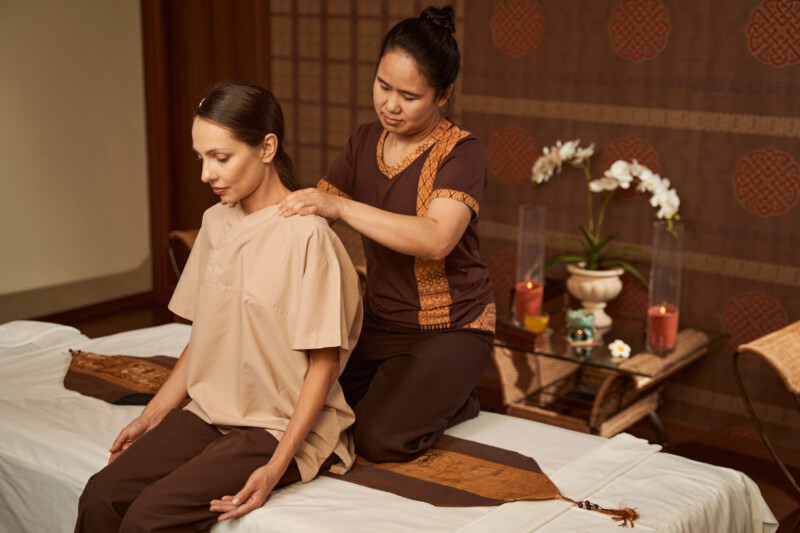 Experienced masseuse working her client upper trapezius region during Thai neck massage