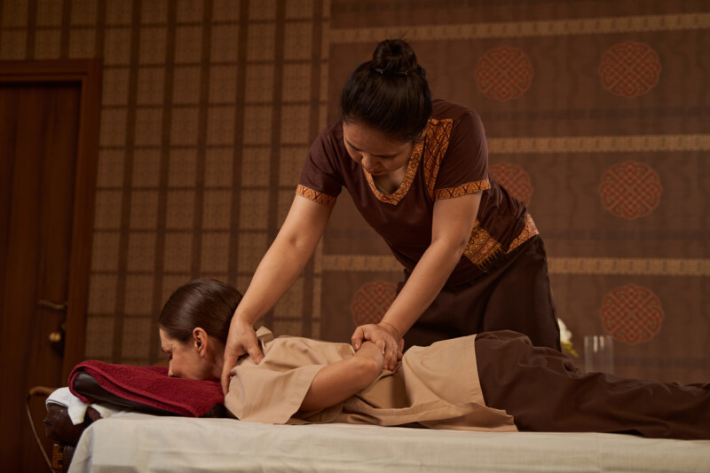 Masseuse thumb pressing trigger point during Thai massage Concentrated serious Asian massotherapist applying pressure to affected muscle on patient shoulder