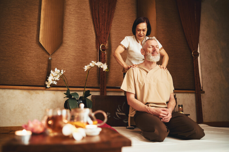 Low angle of Asian woman treating male neck with hands while he is sitting on knees