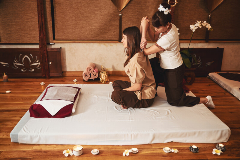 Asian woman wearing flower hair tie bringing client right arm behind her head during muscle massage